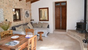 A cozy living room with a wooden dining table, a sofa with patterned cushions, a wooden cabinet, and a stone wall. - Secluded Finca with Private Pool and Extensive Garden in the Campanet valley  (Campanet)