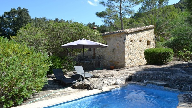 A stone building with a tiled roof, a swimming pool, and two lounge chairs under a patio umbrella. - Secluded Finca with Private Pool and Extensive Garden in the Campanet valley  (Campanet)