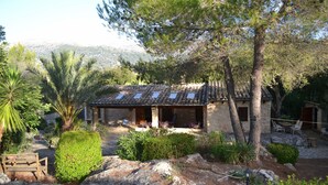 A rustic stone building with a tiled roof, surrounded by lush greenery and a mountainous backdrop. - Secluded Finca with Private Pool and Extensive Garden in the Campanet valley  (Campanet)