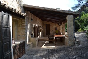 A stone building with a covered patio, a wooden door, and a table with chairs. - Secluded Finca with Private Pool and Extensive Garden in the Campanet valley (Campanet)