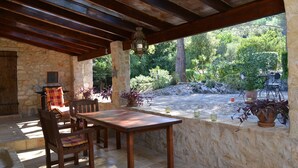 A stone patio with a wooden table and chairs, surrounded by potted plants and a view of a garden. - Secluded Finca with Private Pool and Extensive Garden in the Campanet valley  (Campanet)