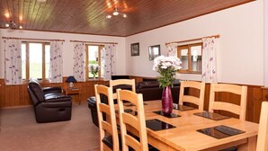 A dining area with a wooden table and chairs, a vase with flowers, and a sofa in the background.