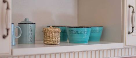 A cabinet shelf with a sugar container, a woven basket, and two dessert cups.