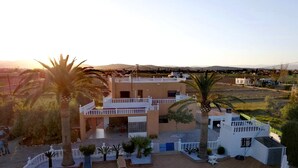 Un edificio de dos pisos con piscina, rodeado de palmeras y vistas al campo.