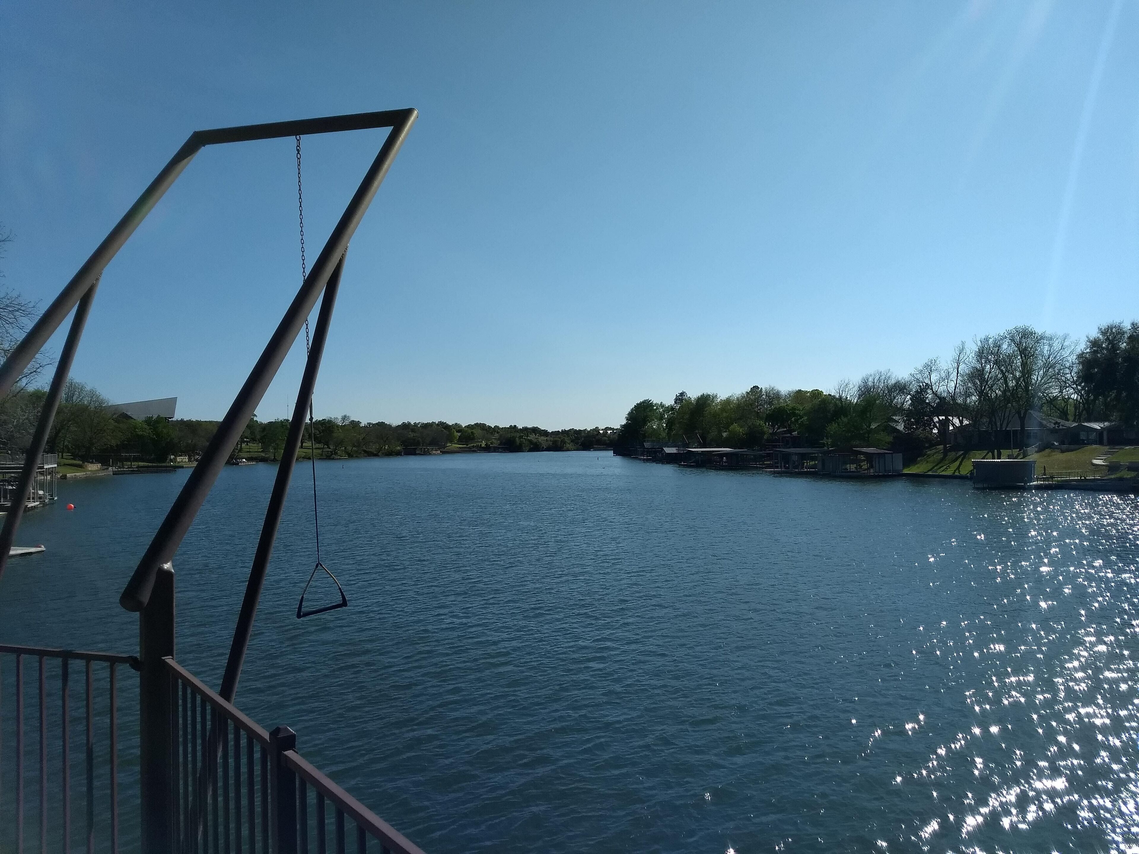 A river with a swing set on a bridge, surrounded by trees and buildings.