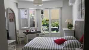 A bedroom with a bed, a desk, chairs, and a window with a view of the garden. - Bright, air-conditioned studio with garden terrace, in the heart of Cannes (Cannes)