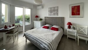 A modern bedroom with a bed, a desk, and a chair. There is a window with a view of greenery outside. - Bright, air-conditioned studio with garden terrace, in the heart of Cannes (Cannes)