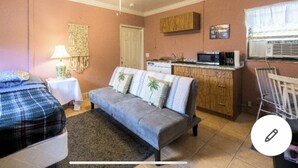Een slaapkamer met twee bedden, een slaapbank, een kleine tafel met lamp, en een keukenhoek met een magnetron en spoelbak.