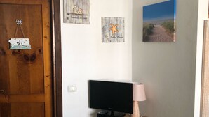 A room with a wooden door, a TV on a wooden stand, a beach painting, and a sign reading "WC". - Rent studio apartment  (La Maddalena)