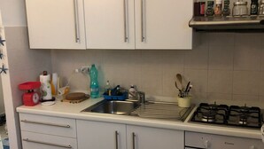 A kitchen with white cabinets, a sink, a stove, and various kitchen items. - Rent studio apartment  (La Maddalena)