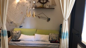 A cozy room with a bed, a wall-mounted shelf with decorative items, and a window with curtains. - Rent studio apartment  (La Maddalena)