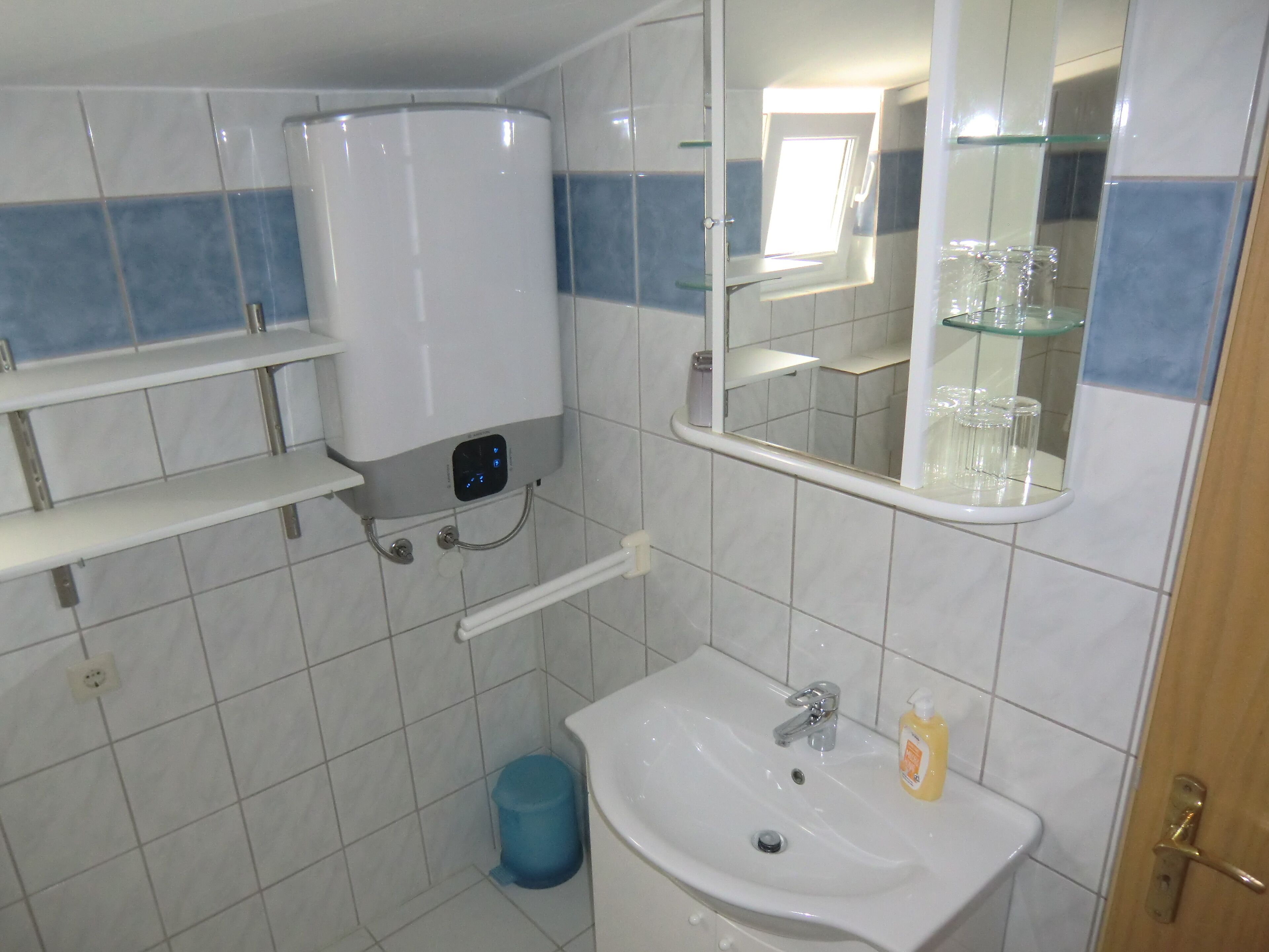 A bathroom with a toilet, sink, mirror, and shelves.