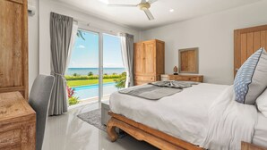 A bedroom with a large bed, wooden wardrobe, and a view of a pool and ocean. - Baan Rim Haad (Koh Samui)