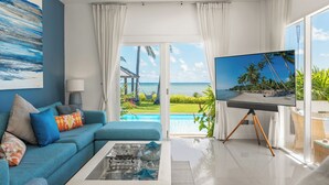 A living room with a large TV, a sofa, a coffee table, and a view of the ocean. - Baan Rim Haad (Koh Samui)