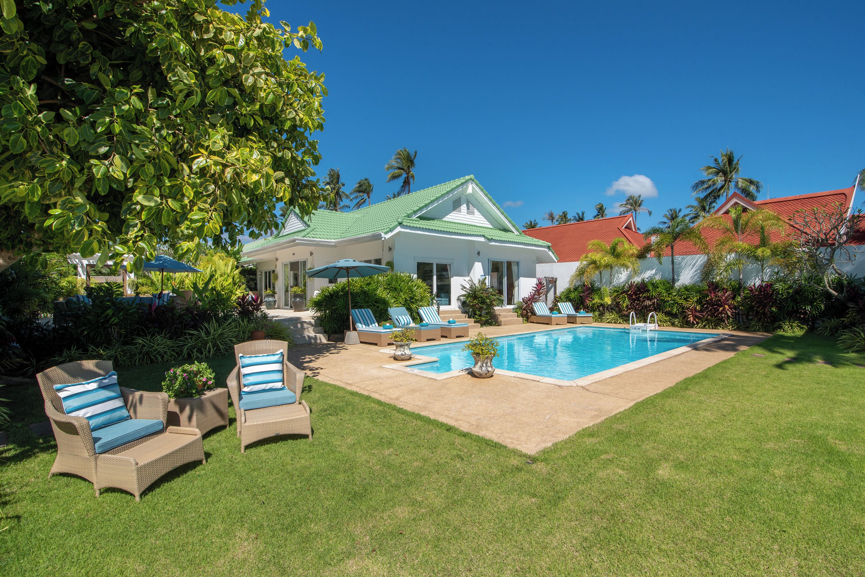 Una casa con piscina, rodeada de césped cuidado y palmeras.
