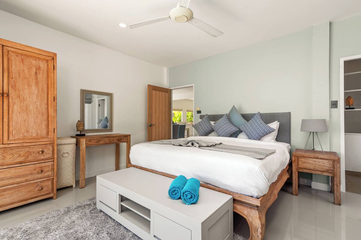 A bedroom with a bed, a wooden wardrobe, a bedside table with a lamp, and a mirror on a dresser.