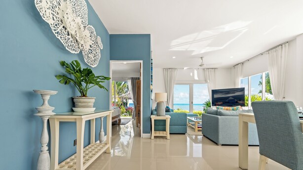A modern living room with a blue accent wall, a white console table with a potted plant, a grey sofa, and a television. - Baan Rim Haad (Koh Samui)