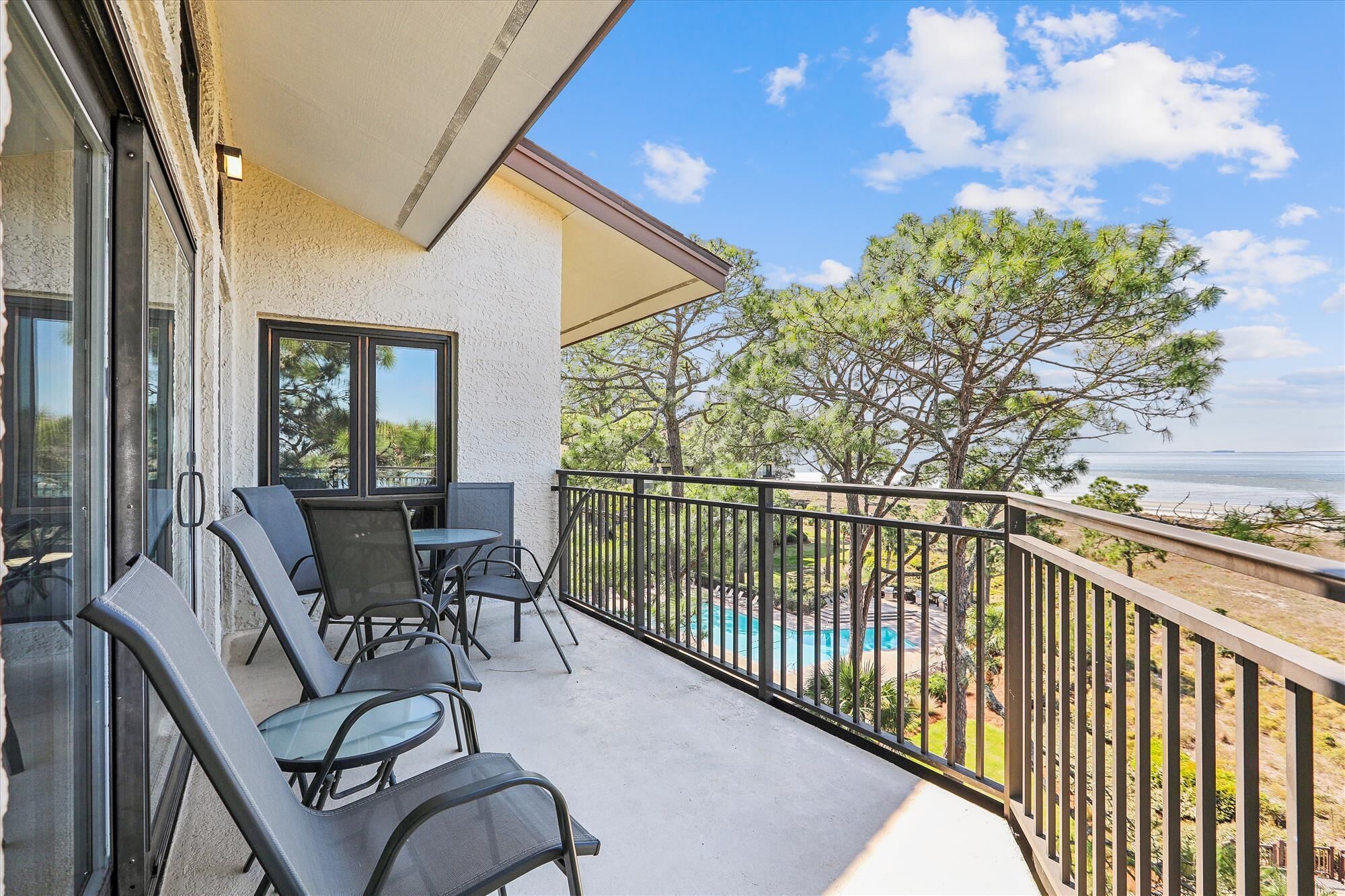A balcony with outdoor seating, a view of the ocean, and a pool area.