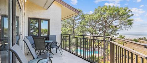 A balcony with outdoor seating, a view of the ocean, and a pool area.