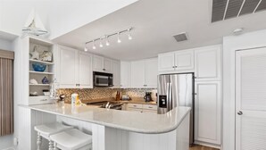 A modern kitchen with white cabinetry, a stainless steel refrigerator, a microwave, and a coffee maker.