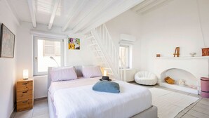 Ein Schlafzimmer mit einem Bett, einem hölzernen Nachttisch, einem weißen Stuhl, einer Treppe und einem kleinen Regal mit Dekoration.
