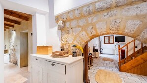 Ein rustikaler Innenraum mit einem Steingewölbe, einer Holztreppe und einer Küchenzeile mit einem weißen Schrank sowie einer gewebten Matte auf dem Boden.