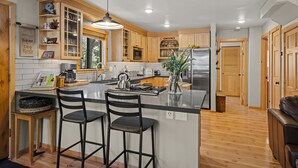Una cocina moderna con armarios de madera, una isla central con taburetes de bar, un refrigerador de acero inoxidable y una lámpara colgante.