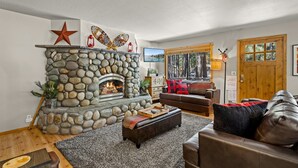 Una sala de estar acogedora con chimenea de piedra, sofás de cuero y un ventanal con vistas al exterior.