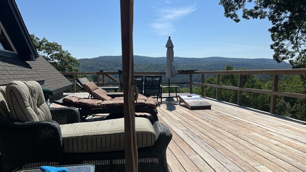 Eine Holzterrasse mit Sitzgelegenheiten im Freien, darunter ein Korbsessel und -stühle sowie ein Tisch mit einem Buch.