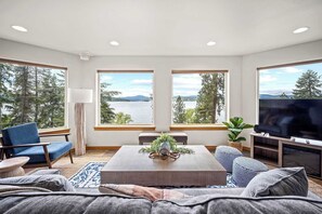 A modern living room with large windows, a flat-screen TV, and comfortable seating. - Lakeview 3BR Home with Hot Tub (Coeur d'Alene)