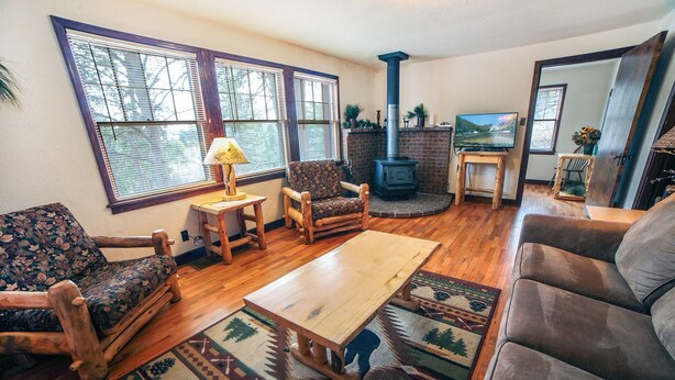A cozy living room with wooden furniture, a fireplace, and large windows. - Stonehaven Home - Perfect for family getaway #3384 (Estes Park)