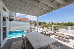 Un espacio exterior techado con piscina, sillas de descanso y una mesa.