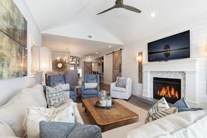 A living room with a fireplace, a ceiling fan, and a TV mounted above it.