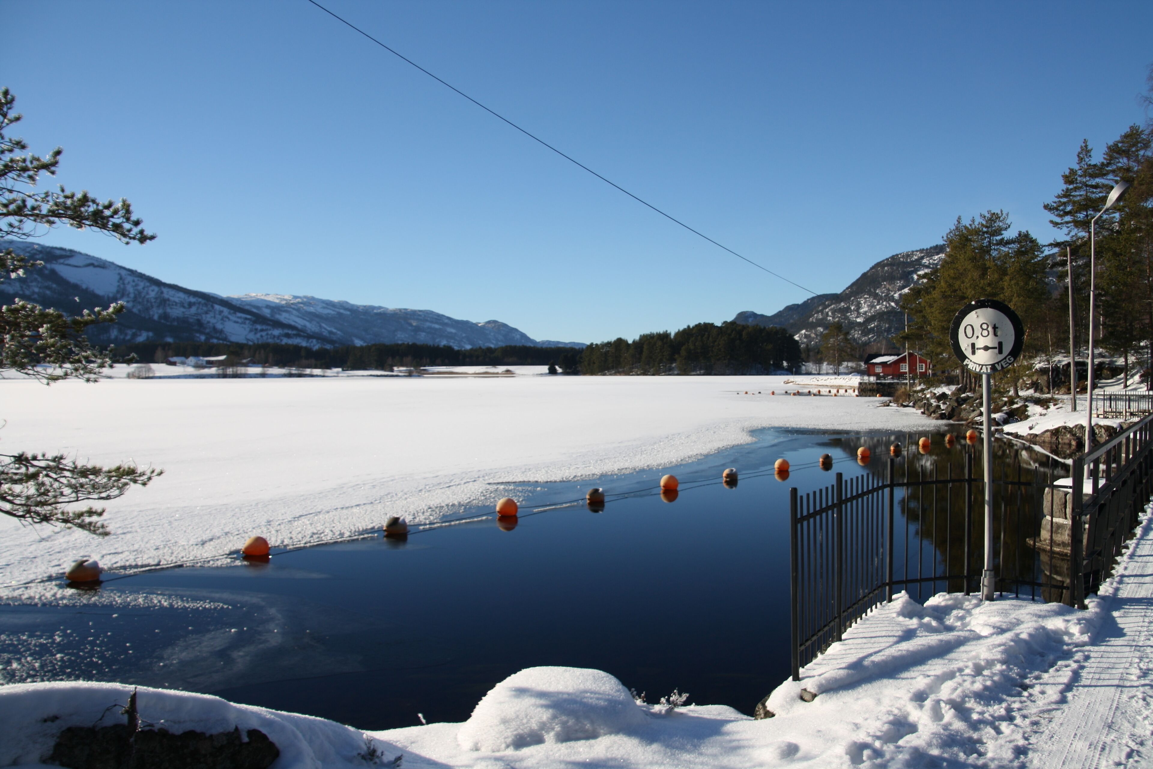 Un paysage enneigé avec un lac gelé, une clôture et un panneau indiquant une pente de 0,8 %.