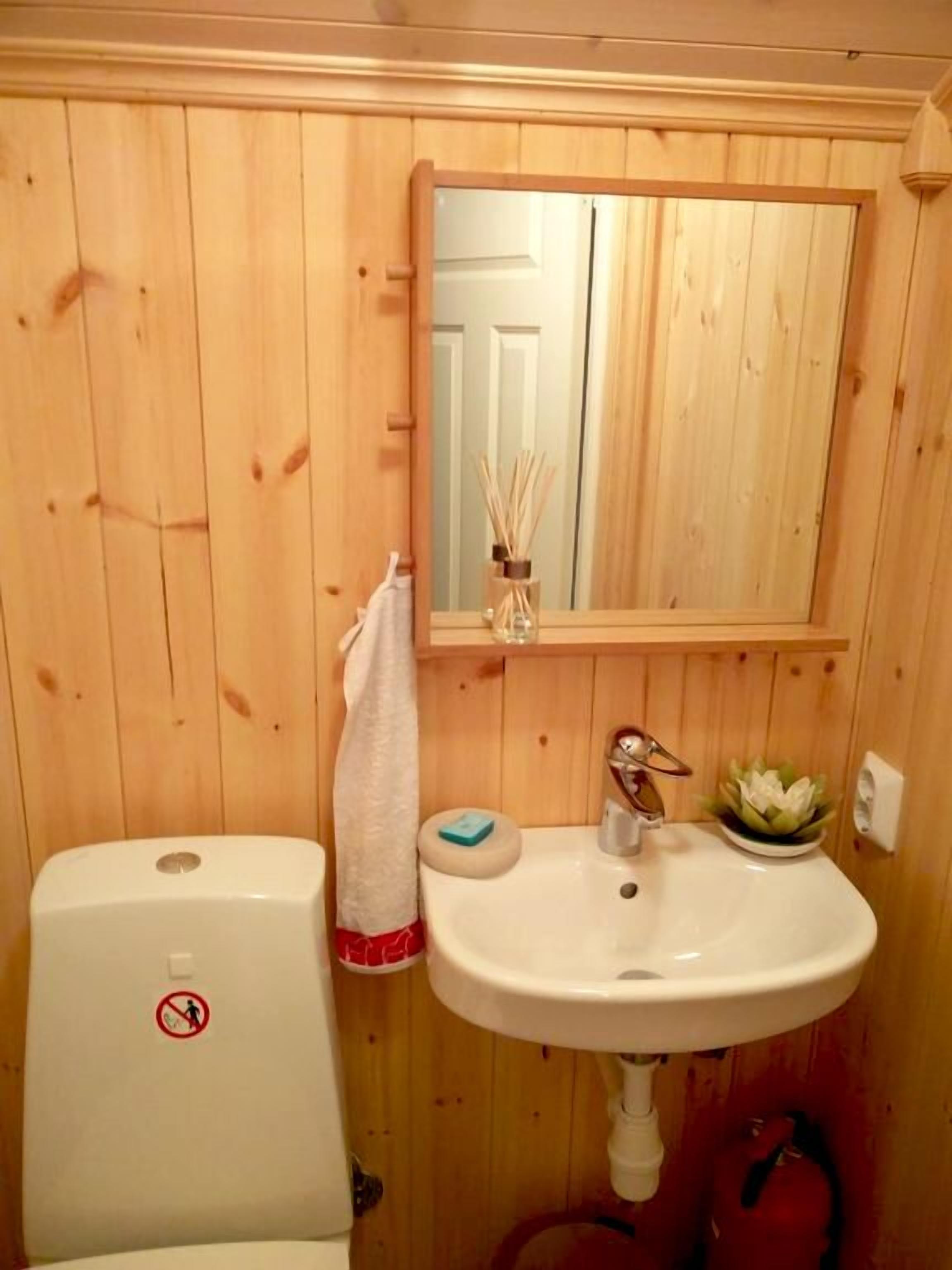 Un bagno con rivestimenti in legno, un water bianco, un lavandino e uno specchio sopra.