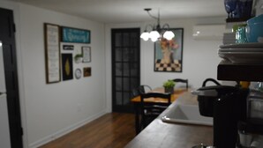 A kitchen with wooden flooring, a dining table, chairs, a coffee machine, and various kitchen utensils.