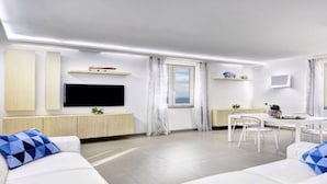 A modern living room with a flat-screen TV, white sofas with patterned cushions, a dining area with a table and chairs, and a window with a view. - A newly renovated, stylish 2 bedroom apartment with amazing sea view (Nerano)