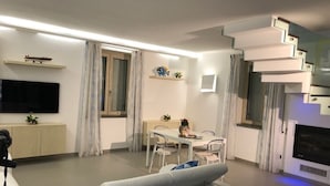 A modern living room with a sofa, dining table, chairs, a flat-screen TV, and a fireplace. - A newly renovated, stylish 2 bedroom apartment with amazing sea view (Nerano)