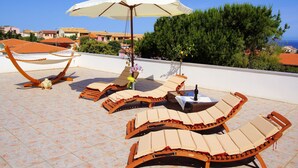 Una terraza en la azotea con sillones de descanso, una sombrilla blanca y una botella de vino.