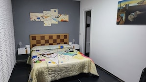 Een slaapkamer met een gestreept hoofdeinde, een bed met een kleurrijke quilt, een abstract schilderij aan de muur en een deur naar een andere kamer.