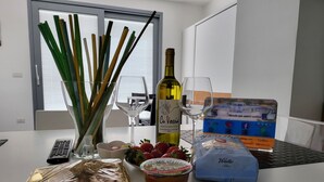 Een tafel met een fles wijn, twee glaasjes, een schaal aardbeien, een broodzak en een laptop met een reisbrochure.