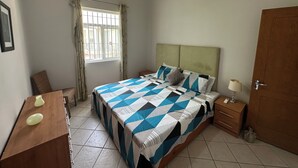 Une chambre à coucher avec un lit, une table de chevet, une lampe et une fenêtre avec des rideaux.