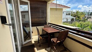 Un balcon avec une table et des chaises, une porte-fenêtre coulissante et une vue sur les bâtiments voisins et la verdure.