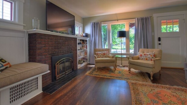 Una sala de estar con chimenea de ladrillo, dos sillones, un sofá y un ventanal con cortinas.