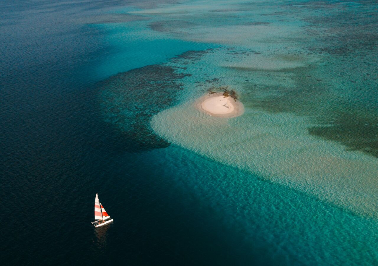 Eine Vogelperspektive auf ein klares türkisblaues Meer mit einer kleinen Insel und einem Segelboot.