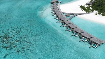 Vista aérea de un complejo turístico con bungalows sobre el agua, conectados por una pasarela curva.