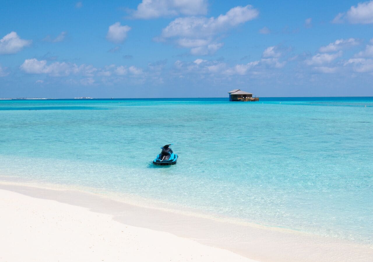 A clear turquoise sea with a white sandy beach and a small boat in the water.