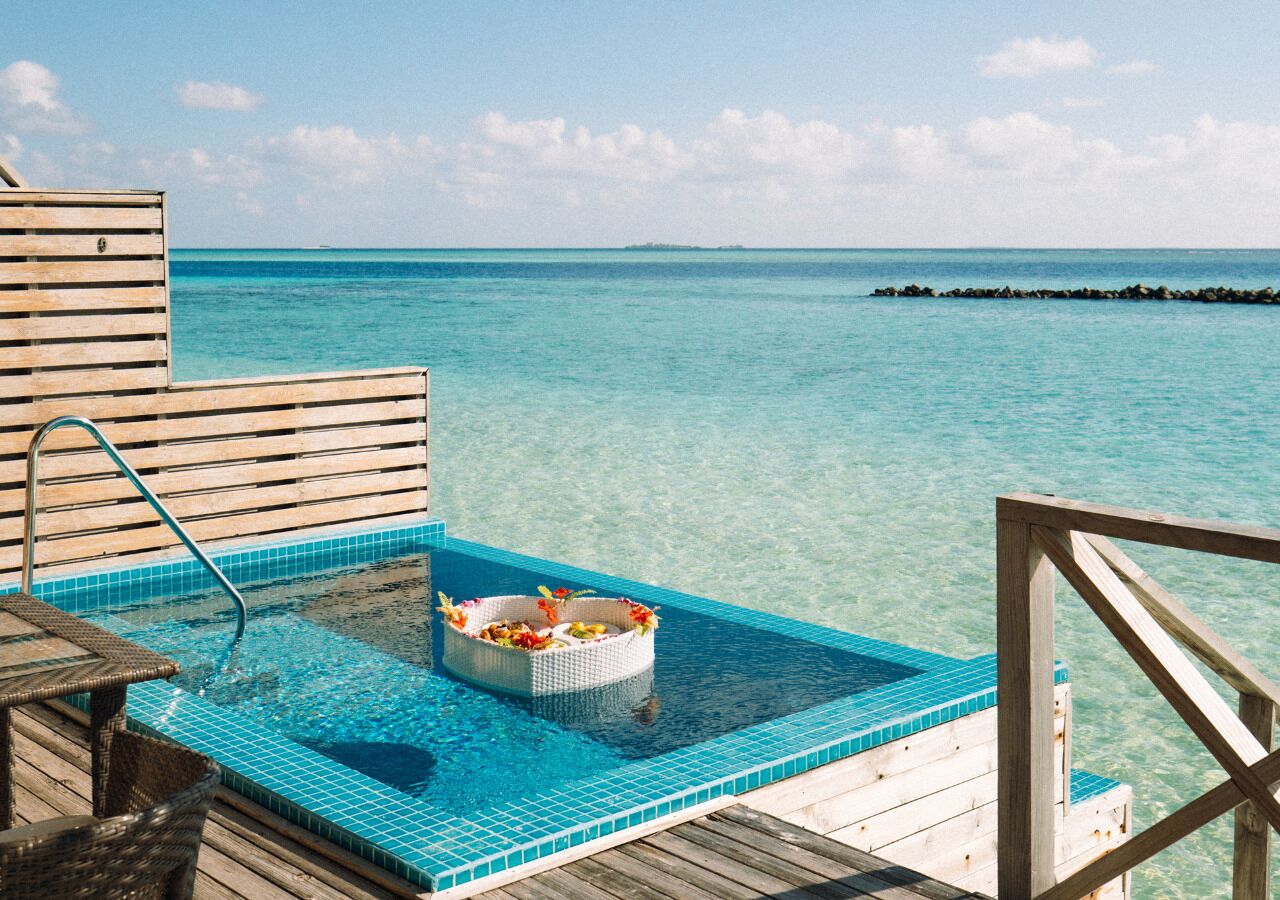 A wooden deck with a pool and a floating basket of fruits.