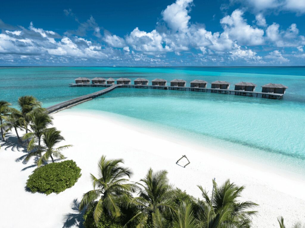 Ein Strandresort mit Bungalows über dem Wasser, einem weißen Sandstrand und klarem türkisblauem Wasser.