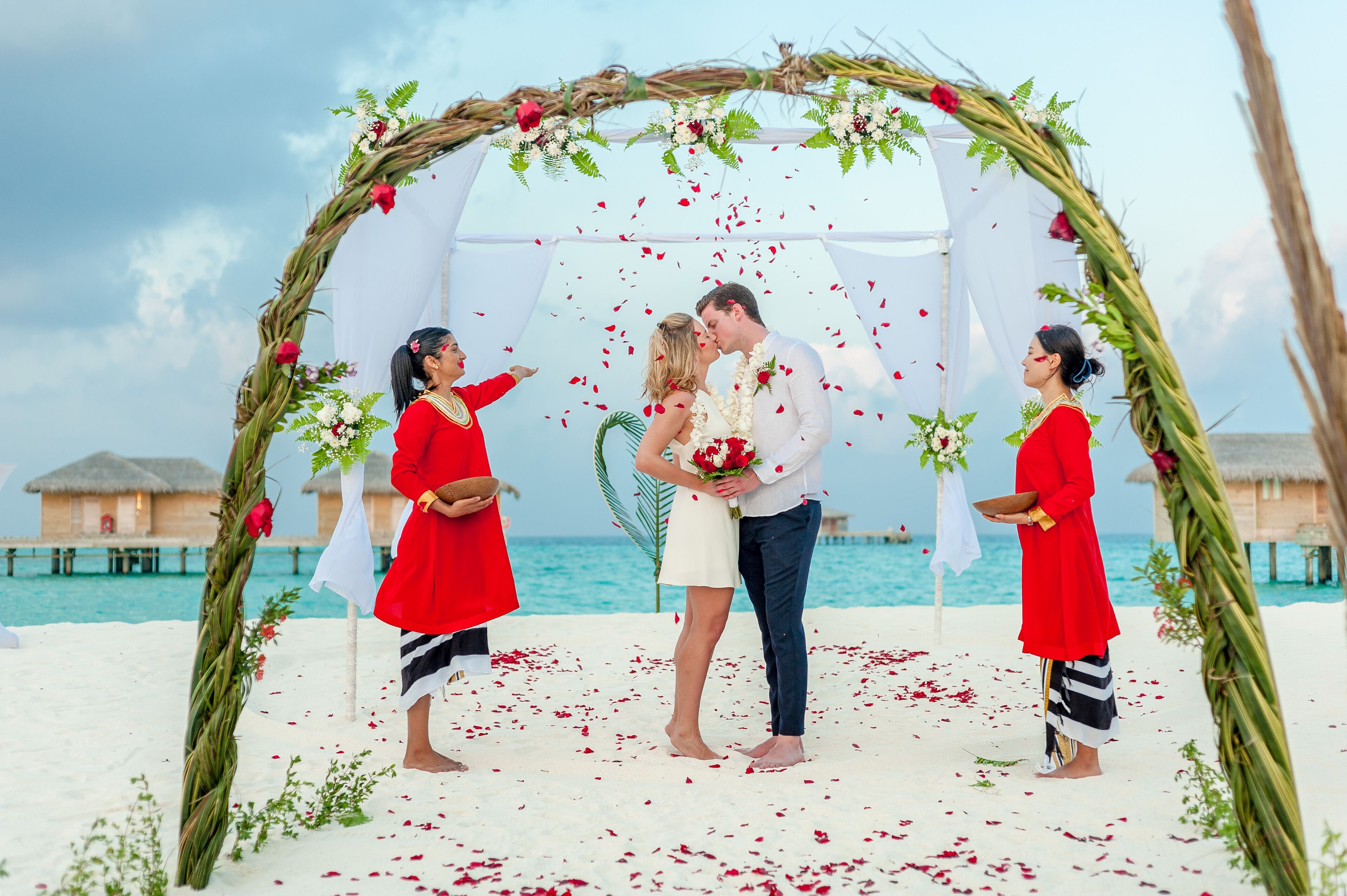 A wedding ceremony on a beach with a white canopy and floral decorations.